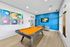 Vibrant recreation room featuring a bold orange pool table, colorful billiard-themed artwork, and a sleek blue accent wall with modern entertainment setup.