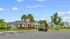 Charming apartment complex exterior with well-maintained landscaping, palm trees, and ample parking space under a bright blue sky.