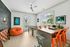 Vibrant playroom featuring a chalkboard wall, bean bag, foosball table, and a bar with bright orange seats, all under a ceiling fan with ample natural light.