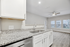 Modern kitchen with sleek granite countertops and white cabinetry, opening into a bright living area with wood flooring and large windows.