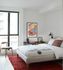 Modern bedroom with elegant decor, featuring a large window, cozy bed, stylish red rug, and chic art on the wall.