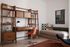 Chic home office with a mid-century modern wooden desk, vibrant orange chair, and stylish shelving. Cozy sofa with patterned cushions adds a touch of comfort.