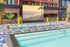Chic urban apartment complex featuring a stylish outdoor pool, vibrant tiled deck, and lush greenery with a sunset beach scene mural.