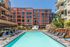 Vibrant urban apartment complex with a stunning outdoor pool, palm trees, and luxurious lounge chairs, perfect for modern living.
