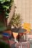 Charming outdoor patio with colorful chairs, lush potted plants, and a stylish black table against a modern brick wall.