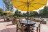 Charming outdoor patio with elegant seating under vibrant yellow umbrellas, surrounded by lush greenery and a tennis court.