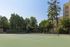Beautiful outdoor tennis court surrounded by lush greenery and modern apartment buildings under a clear blue sky.
