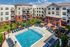 Luxurious apartment complex featuring a sparkling swimming pool, comfortable sun loungers, and vibrant garden landscaping, promising a relaxing and stylish outdoor experience.