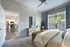 Bright and airy bedroom with modern decor, large window, and open view into a stylish kitchen with stainless steel appliances.