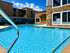 Luxurious apartment complex with sparkling blue swimming pool, surrounded by elegant stone architecture under a sunny sky.