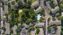 Breathtaking aerial view of a well-planned apartment complex featuring a lush central park, large shimmering pool, and ample parking spaces surrounded by vibrant greenery.