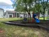 Charming residential community with a vibrant playground featuring a blue slide, surrounded by lush trees and a modern clubhouse.