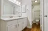 Elegant bathroom featuring a double vanity with sleek fixtures, spacious mirror, and warm wood flooring, leading to a cozy shower area.