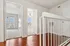 Bright, airy hallway with polished wood-style floors leading to sunlit rooms, featuring elegant doors and modern white railing.