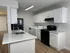 Sleek modern kitchen with white cabinetry and black appliances, featuring a spacious quartz countertop and built-in washing facilities.