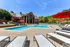Luxurious outdoor pool area with stylish lounge chairs, vibrant red umbrellas, and a stunning brick building under a clear blue sky.