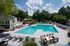 Lush apartment community pool area with spacious lounge chairs, vibrant playground, and outdoor grills surrounded by greenery.