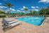 Inviting pool area with comfortable lounge chairs and vibrant umbrellas, surrounded by lush palm trees under a bright blue sky.