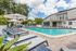 Inviting outdoor pool area surrounded by comfortable lounge chairs and umbrellas, set against a backdrop of lush greenery and a modern building under a bright, blue sky.