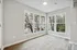 Bright corner room with large, sunlit windows offering peaceful views of trees, featuring elegant hardwood floors and a modern light fixture.