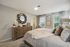Elegant bedroom with plush bedding, accented by a stylish dresser and modern decor, featuring large windows that invite natural light and a serene ambiance.