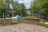 Charming outdoor space featuring a stone BBQ grill under a stylish pergola, surrounded by lush greenery and inviting poolside seating with vibrant umbrellas.