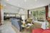 Bright and elegant living area with a modern design, featuring a plush blue sectional sofa, stylish patterned rug, and large windows showcasing a scenic view of a pool and lush greenery.