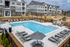 Modern apartment complex with a sparkling outdoor pool, surrounded by elegant lounge chairs and shaded tables, offering a perfect blend of relaxation and luxury living.