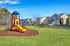 Vibrant community playground with colorful play structures surrounded by beautiful suburban homes, perfect for family-friendly living.