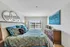 Bright and inviting bedroom with a large window, stylish teal bedding, elegant wooden dresser, and contemporary artwork.