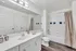 Modern bathroom featuring sleek white cabinetry, a large mirror, a bathtub with chic tiling, and stylish lighting.