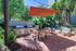 Inviting outdoor patio featuring a modern dining area with an orange umbrella, stylish seating, lush greenery, and built-in grills.