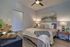 Elegant bedroom with stylish decor, featuring a cozy bed, modern art, and warm ambient lighting on wooden flooring.