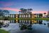 Charming lakefront apartment building at dusk, beautifully lit with reflections in the water and surrounded by lush trees.