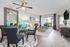 Bright and modern living room with elegant decor, featuring a glass-top dining table, stylish gray chairs, and a cozy seating area with colorful accents, opening to a scenic garden view.