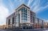Modern multi-story apartment building with large windows and stylish facade under a clear blue sky, corner view showcasing vibrant urban living.
