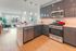 Modern kitchen with sleek gray cabinets, stainless steel appliances, and a bright open-concept living area with large windows.