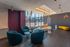 Chic apartment lobby featuring modern blue chairs, stylish white and yellow cushioned seating, and elegant pendant lighting with a vibrant purple accent wall.