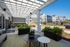 Charming apartment patio with cozy seating and vibrant greenery, offering a stunning view of modern apartment buildings and a pristine community pool.