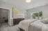 Bright and inviting bedroom featuring a plush bed, chic dresser, modern artwork, and a scenic view through large windows.