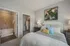 Elegant bedroom featuring stylish bedding, modern nightstands, an abstract painting, and a private walk-in closet with an adjacent luxurious bathroom.
