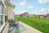 Charming backyard patio with stylish outdoor furniture overlooking well-maintained green space and modern homes under a clear blue sky.