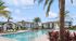 Inviting apartment complex with a stunning outdoor pool, surrounded by lush palm trees and elegant loungers under blue umbrellas.