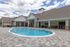 Charming outdoor pool area with elegant patio seating, surrounded by a beautiful clubhouse, perfect for relaxation and entertainment.