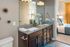 Elegant bathroom with dual sinks, granite countertop, and stylish decor, leading to a cozy bedroom with plush bedding and warm lighting.