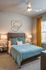 Chic bedroom with modern decor, featuring a plush blue comforter, stylish wall art, and bright natural light from large windows.