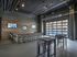 Chic modern open-plan lounge area with an industrial aesthetic, featuring a stylish bar counter, flat-screen TVs, and large glass doors opening to a pool view.