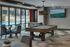 Luxurious entertainment room with a pool table, foosball, modern seating, and expansive pool views through large glass windows.