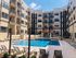 Modern apartment complex with inviting pool area, surrounded by stylish balconies and sun loungers under a clear blue sky.