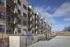 Modern apartment complex with spacious balconies, outdoor grill area, and scenic surroundings under a clear blue sky.